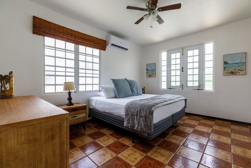 A bright and airy king bedroom at Casa Bonita, featuring plush white luxury linens, tropical decor, and ample natural light, epitomizing the five-star comfort of a high-end vacation rental.