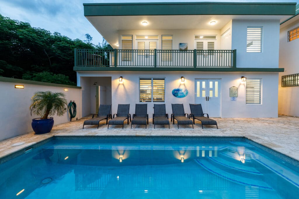 Six modern lounge chairs lined up beside a sparkling turquoise pool at a contemporary luxury villa, reflecting the tranquil and exclusive atmosphere of a private Rincon retreat.
